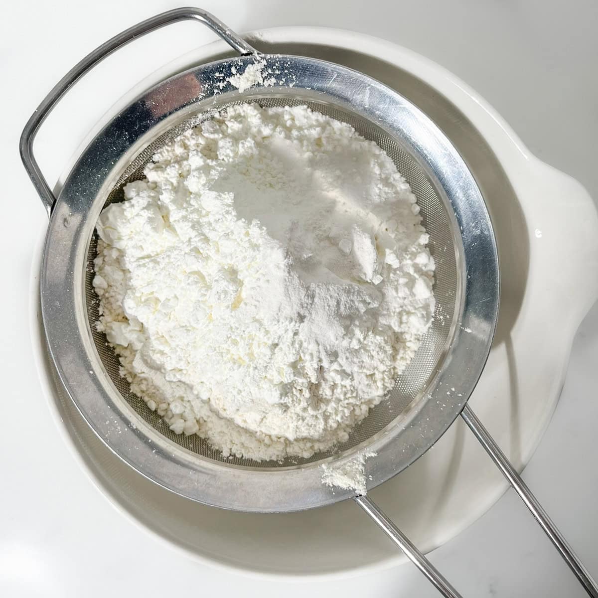 Sifted plain flour, cornflour, baking powder and salt in a sieve over a white mixing bowl.