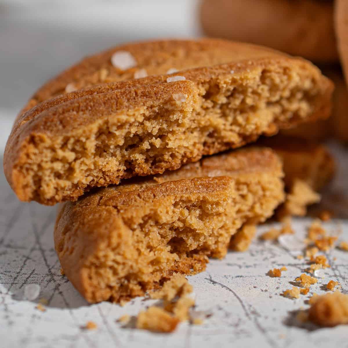 Close-up of the crumb inside a broken caramel condensed milk cookie with flaky sea salt and a stack of cookies in the background.