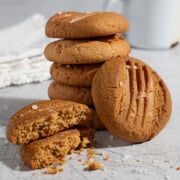 Stack of caramel condensed milk cookies with flaky sea salt, including one broken cookie showing the crumb and a white enamel mug in the background.