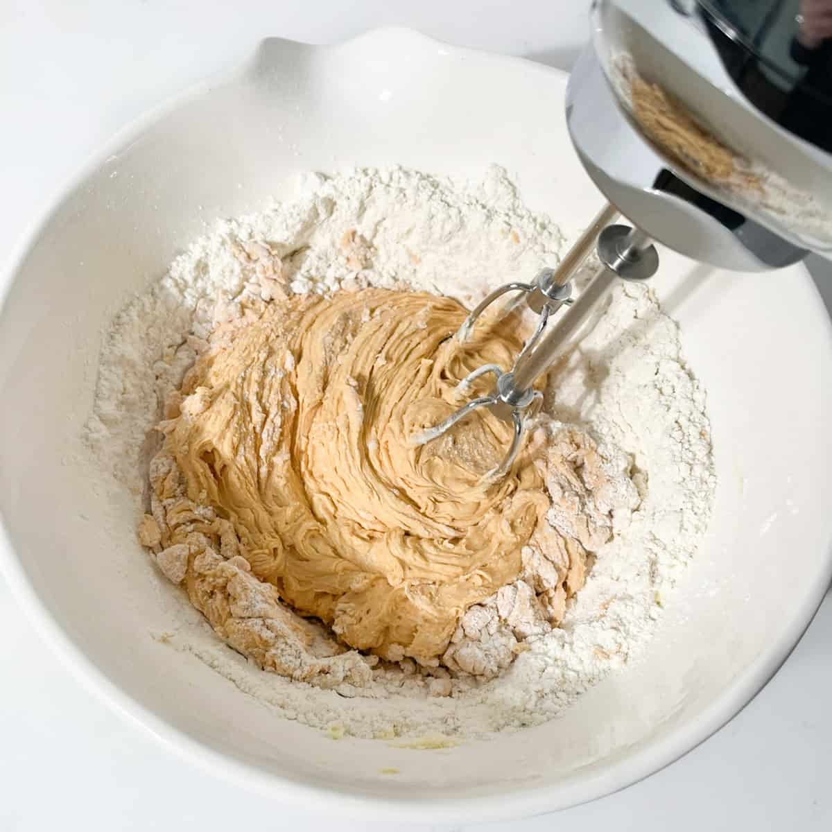 Dry ingredients being added to the caramel butter mixture in a white mixing bowl.