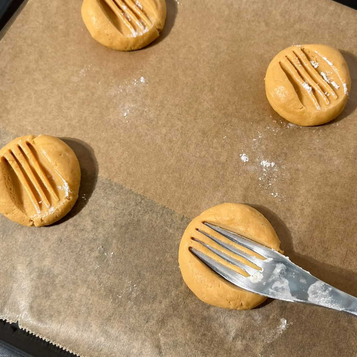 Caramel condensed milk cookie dough rolled into balls, pressed with a fork and arranged on a lined baking tray ready to bake.
