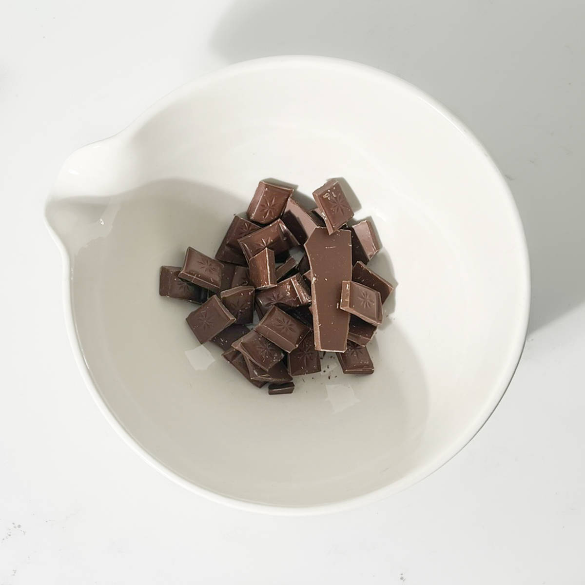 Broken up chocolate in a large white bowl.
