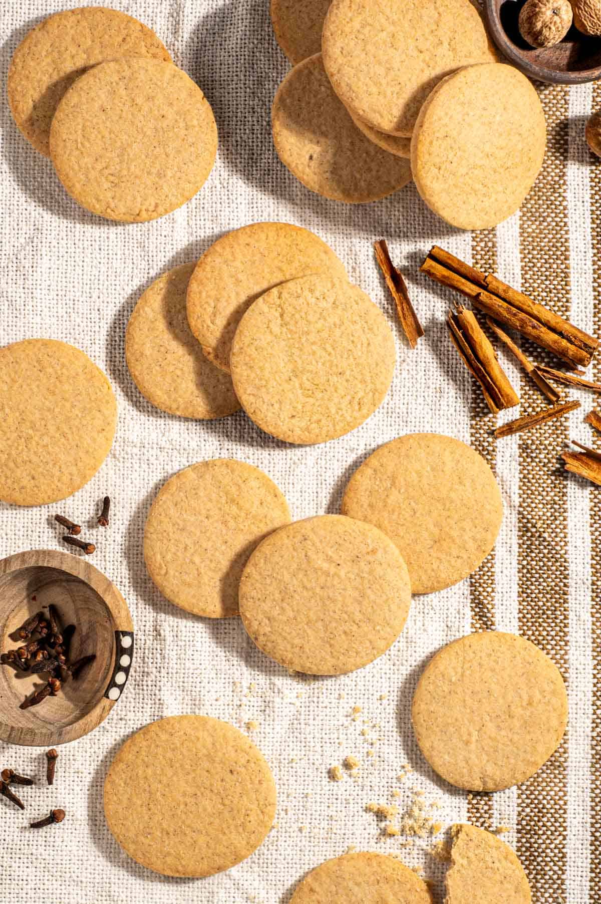 Outydse soetkoekies scattered across a textured tea towel, surrounded by nutmeg, cloves and cinnamon sticks.