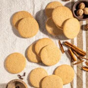 Outydse soetkoekies scattered across a textured tea towel, surrounded by nutmeg, cloves and cinnamon sticks.