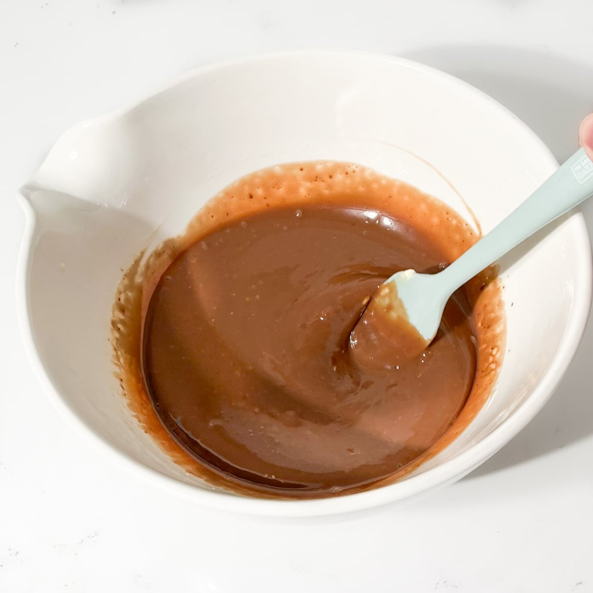 Stirring the cream and the chocolate together in a large white bowl.