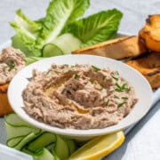 A bowl of tuna pate surrounded by toasted baguette, cucumber ribbons and lettuce.