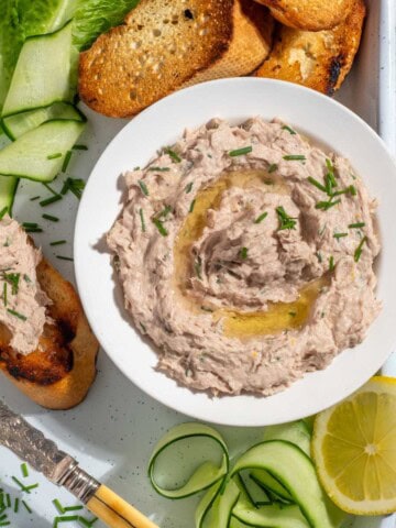 A bowl of tuna pate surrounded by toasted baguette, cucumber ribbons and lettuce.