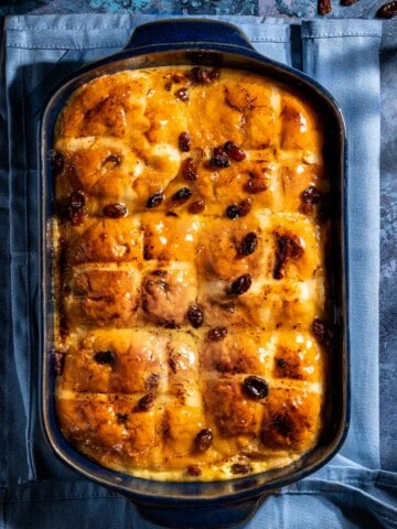 A hot cross bun bread and butter pudding in a blue baking dish, on a blue background.