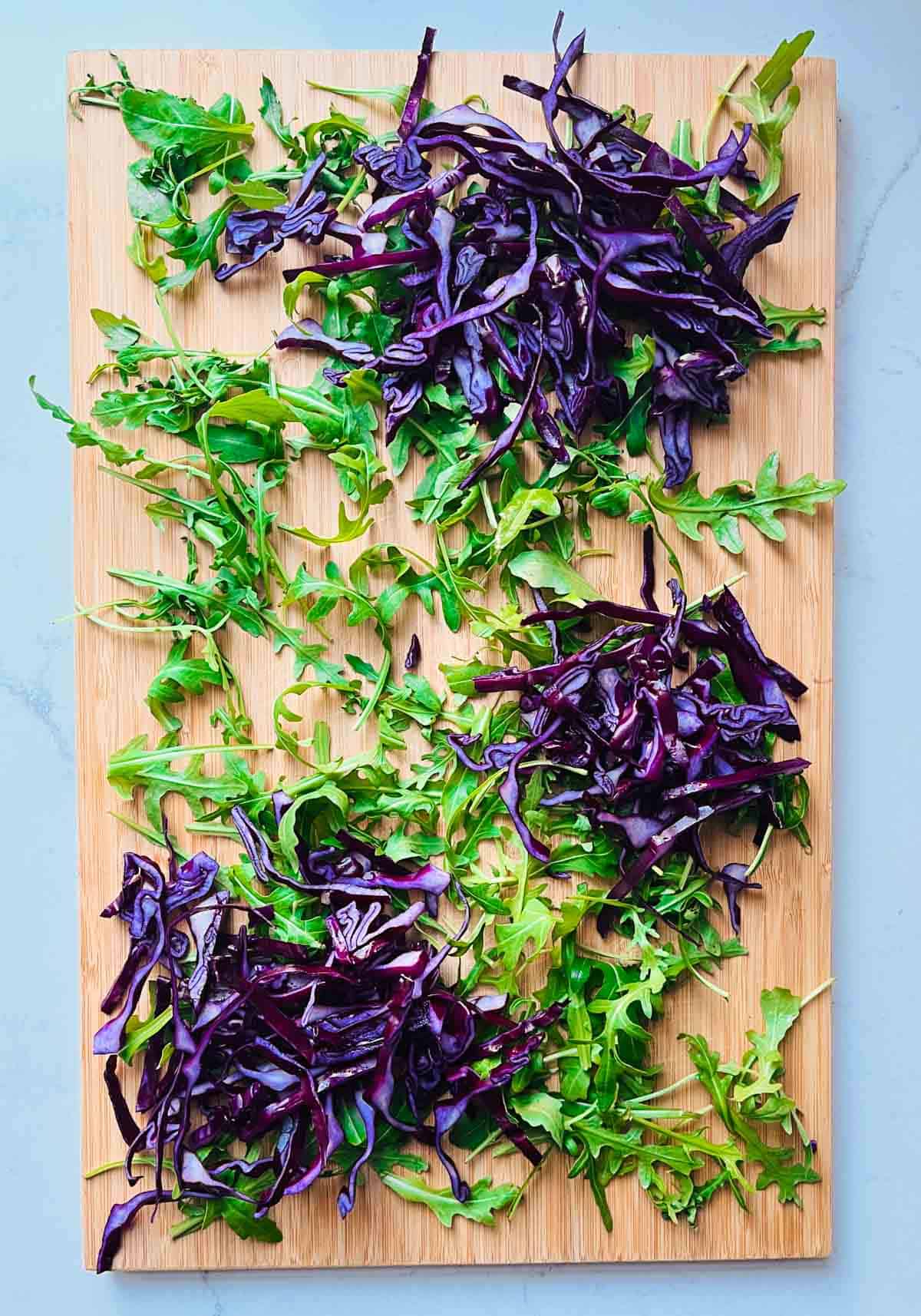 Rocket leaves and chopped red cabbage on a wooded board.