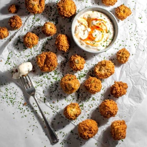 Crumbed mushrooms scattered across baking paper with sweet chilli mayonnaise sauce in a small bowl.