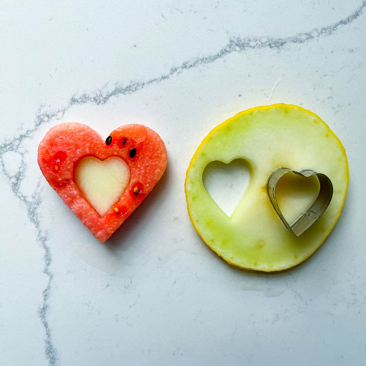 A small heart shaped piece of melon inside a larger heart shaped piece of watermlon.
