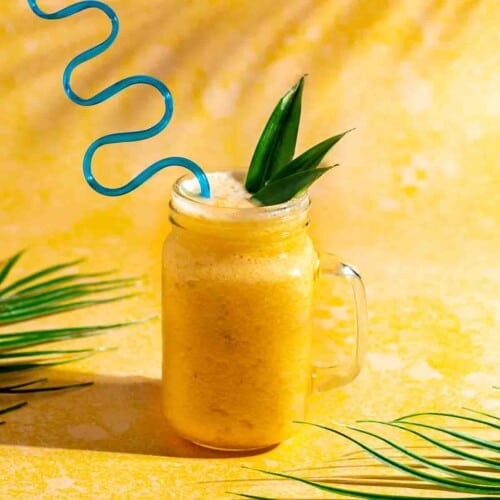 Pineapple slushie in a mason jar with a blue silly straw.
