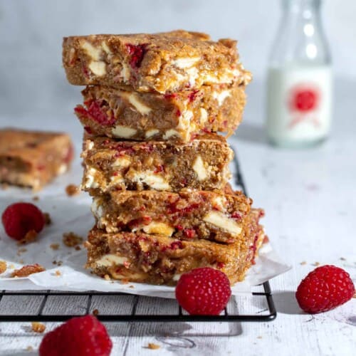 A stack of raspberry and white chocolate blondies on a black cooling rack.