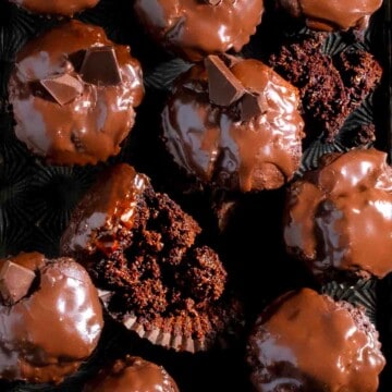 Triple chocolate muffins on a baking sheet with one muffin broken open and laid on its side.