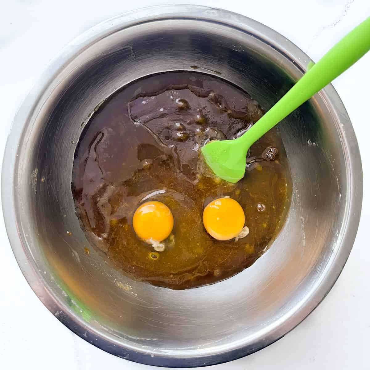 Adding eggs to butter and sugar in a stainless steel bowl.