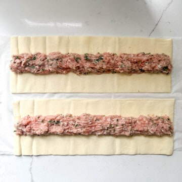 Chicken sausage rolls mixture divided onto two strips of puff pastry.