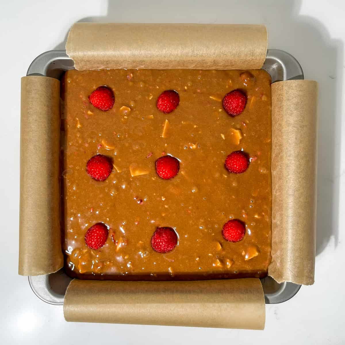 Unbaked raspberry and white chocolate blondies in a square pan.