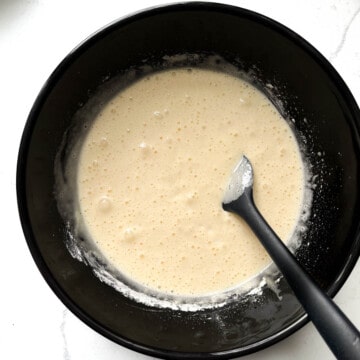 Adding buttermilk to batter in a black bowl.