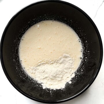 Adding the first third of flour to the egg mixture in a black mixing bowl.