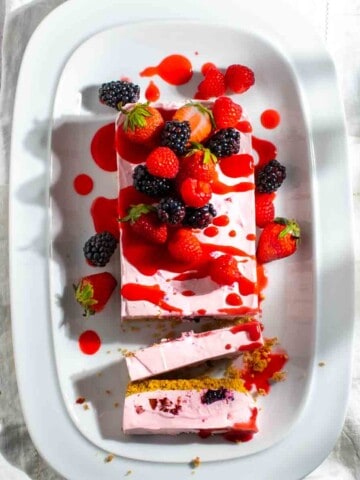 Berry cheesecake on a white serving plate with two slices sliced from it.