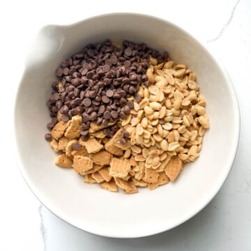 A bowl with crushed biscuits and added chocolate chips an peanuts.