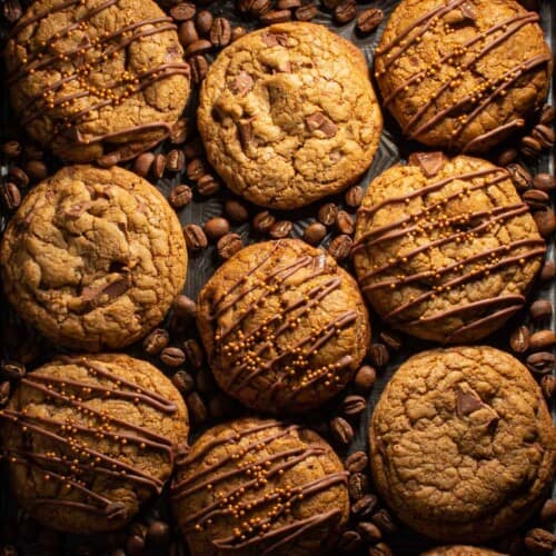 Coffee cookies on a baking tray with coffee beans scattered between cookies.