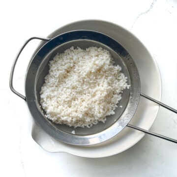 Rinsed sushi rice in a sieve over a bowl to drain the water.