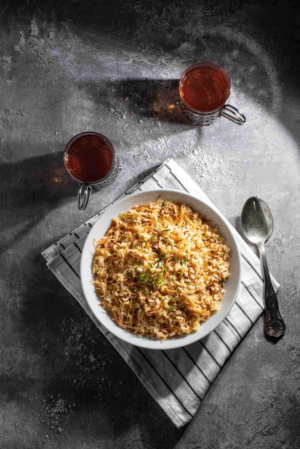 Egyptian rice in a white bowl with two cups of tea in glass mugs.