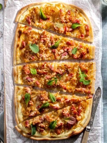 Flammkuchen on a wooden table, sliced into slices.