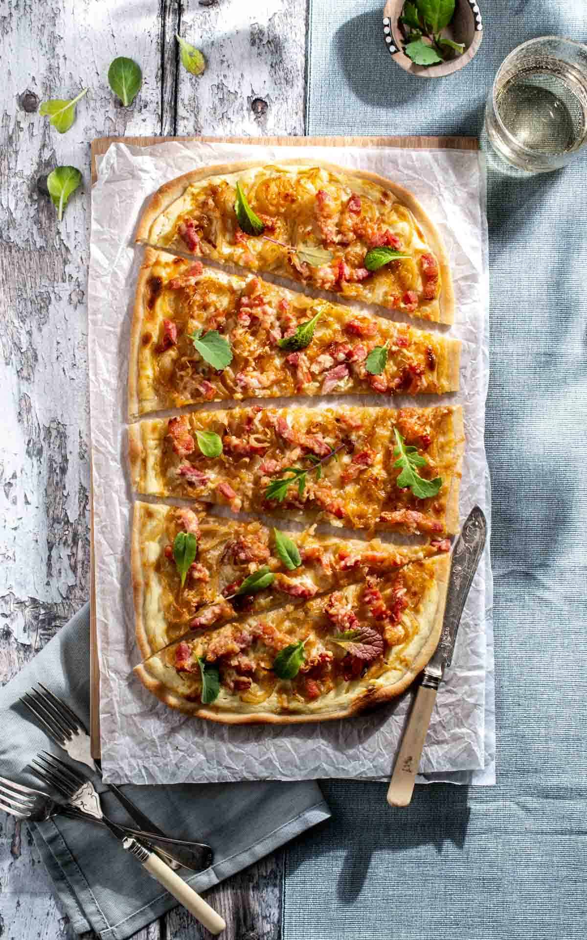 Flammkuchen on a wooden table, sliced into slices.