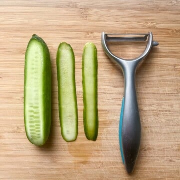 Strips of baby cucumber sliced with a potato peeler on a chopping board.