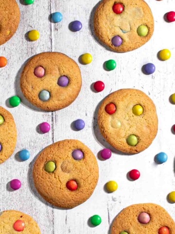 Smartie cookies on a white background with scattered Smarties between the cookies.