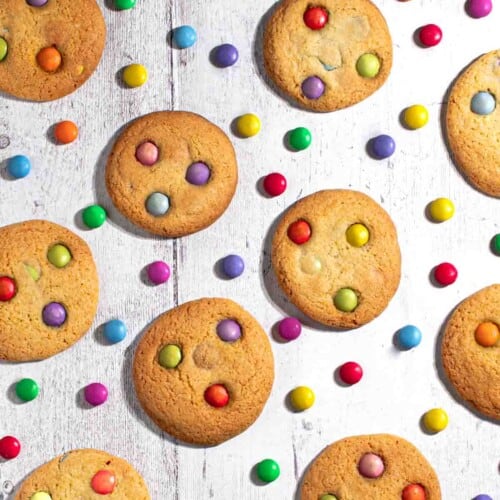 Smartie cookies on a white background with scattered Smarties between the cookies.