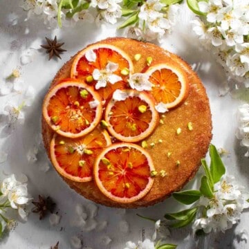 Tunisian cake with sliced oranges on top, surrounded by blossoms.