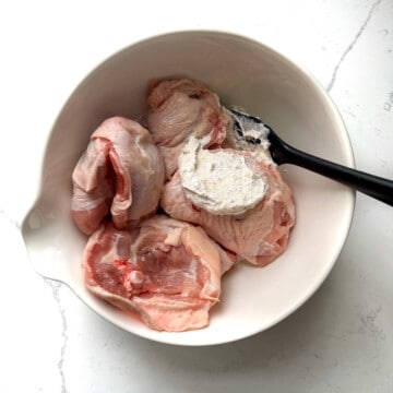 Adding chicken to a bowl with yoghurt marinade.