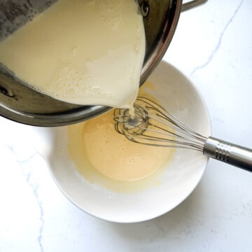 Pouring a quarter of the milk into the eggs in a large mixing bowl.