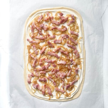 Unbaked flammkuchen with bacon and onions.