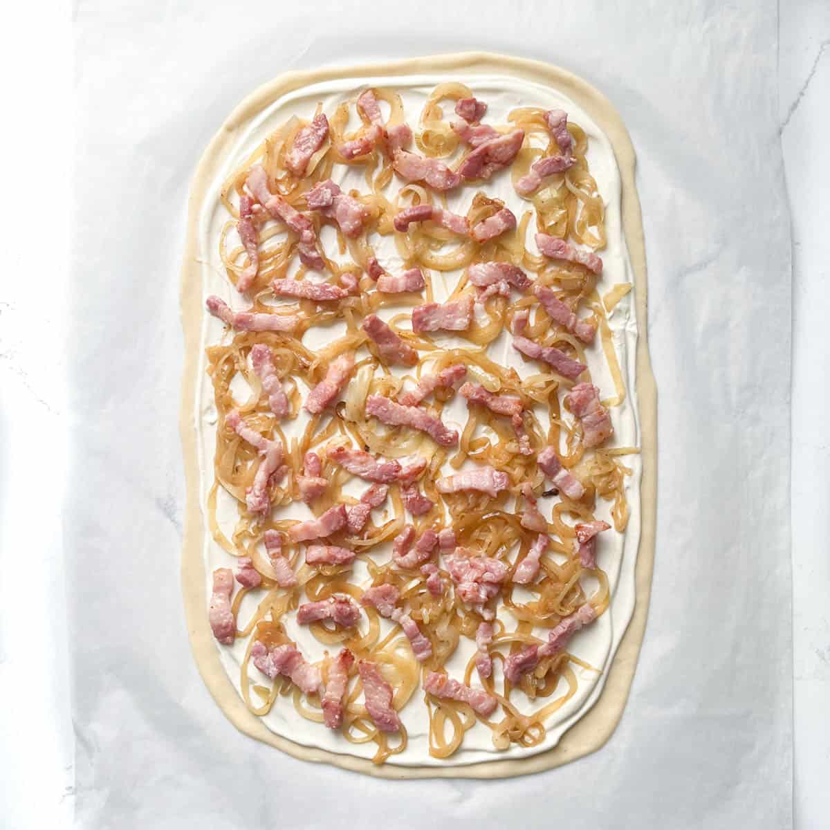 Unbaked flammkuchen with bacon and onions.