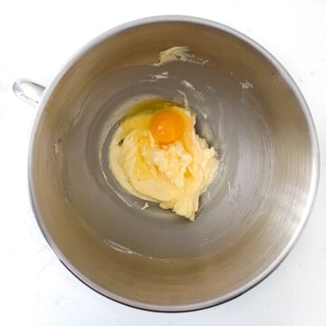 Adding one egg to the butter mixture in the bowl of a stand mixer.