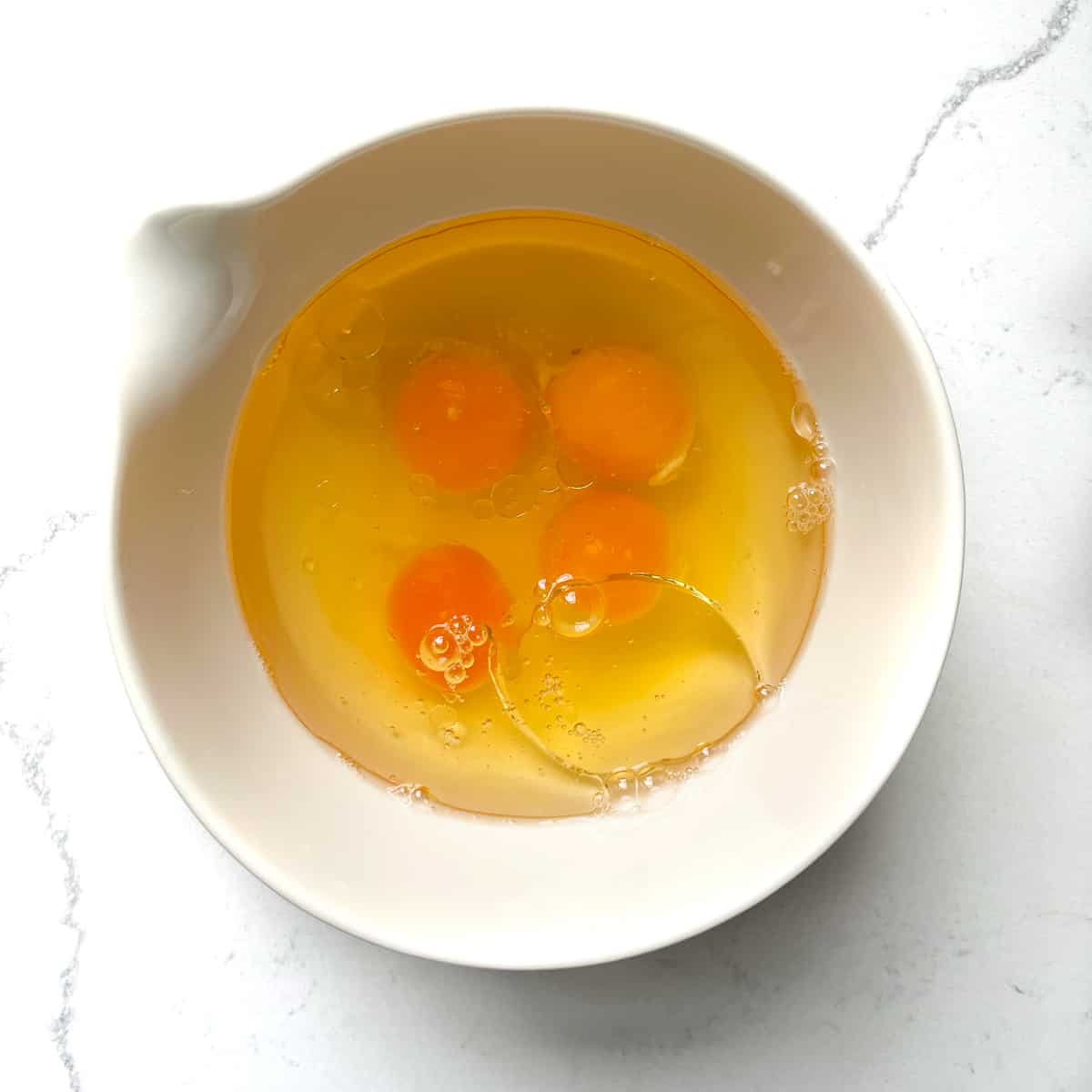 Eggs and oil added to a white bowl.
