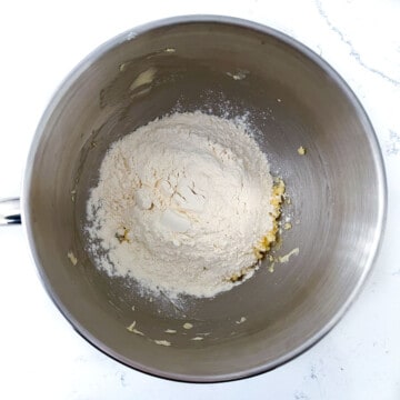 Adding flour to the eggs and butter in the bowl of a stand mixer.