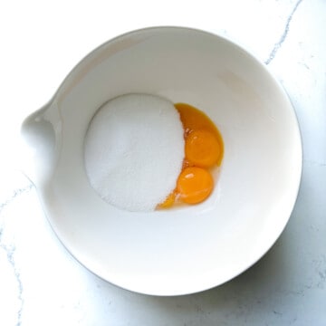 Adding sugar and eggs to a small white bowl.