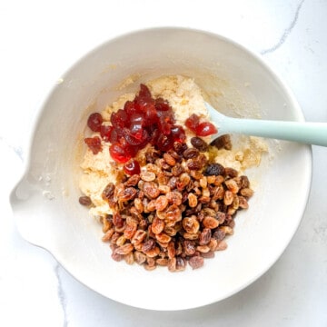 Sultanas and cherries added to cake batter in a white mixing bowl.