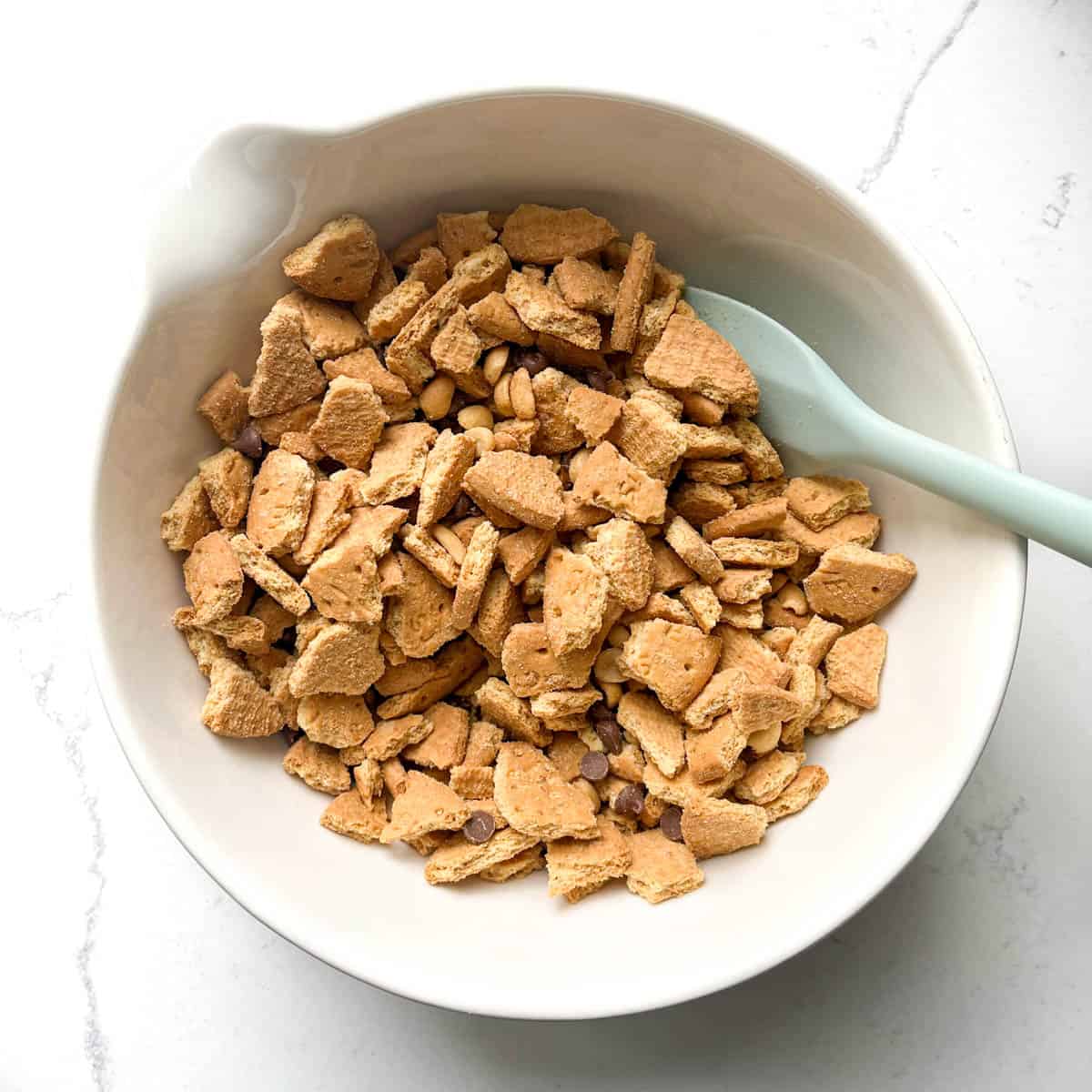 Crushed biscuits in a large white bowl mixed with peanuts and chocolate chips.