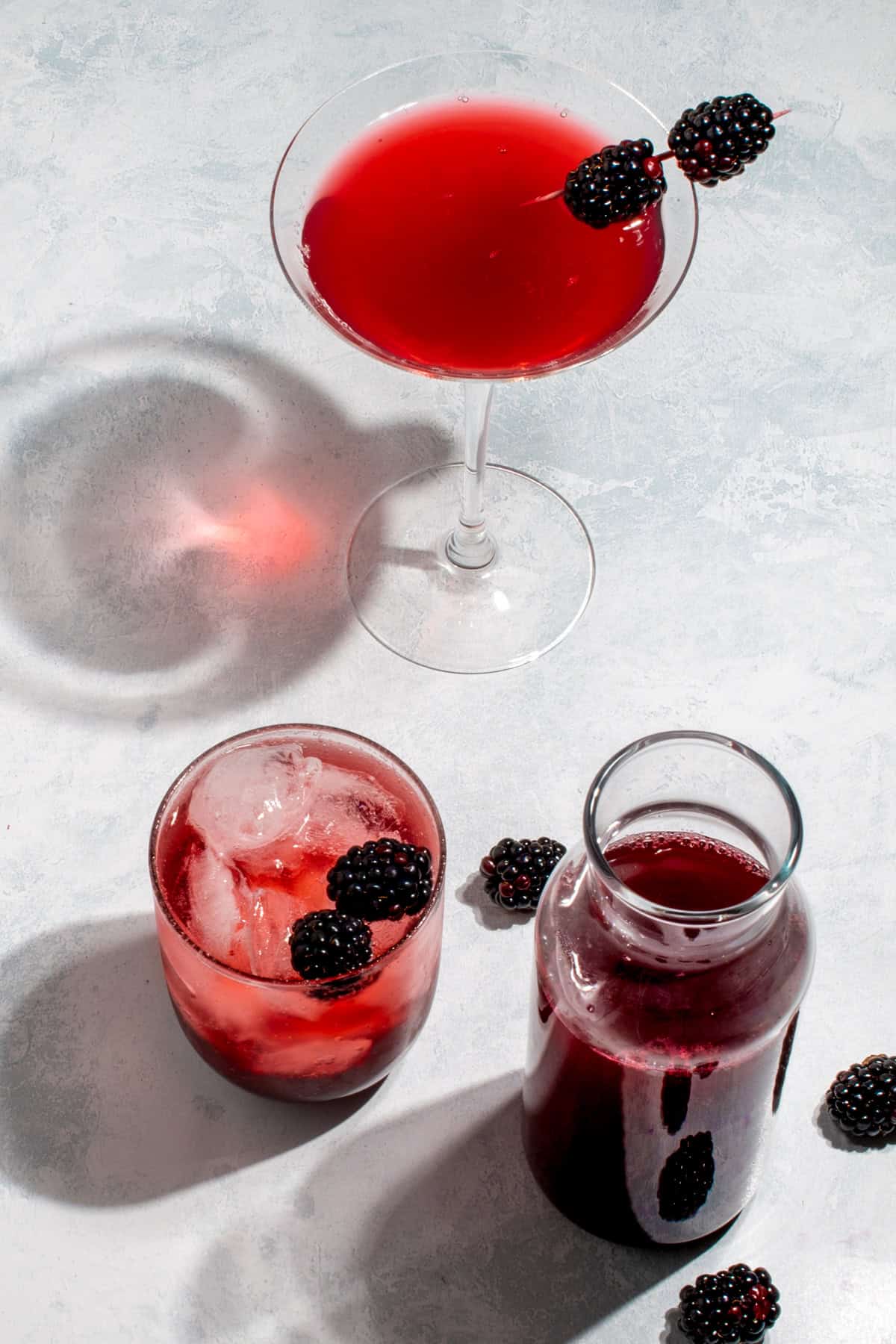 A jar, a glass and a cocktail glass with blackberry simple syrup.