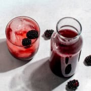 A jar, a glass and a cocktail glass with blackberry simple syrup.