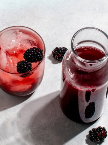 A jar, a glass and a cocktail glass with blackberry simple syrup.