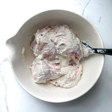 Covering the chicken thighs with the yoghurt marinade in a large white bowl.