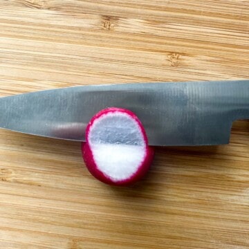 Demonstrating how to slice paper thin radishes with a knife blade slicing halfway through a radish.