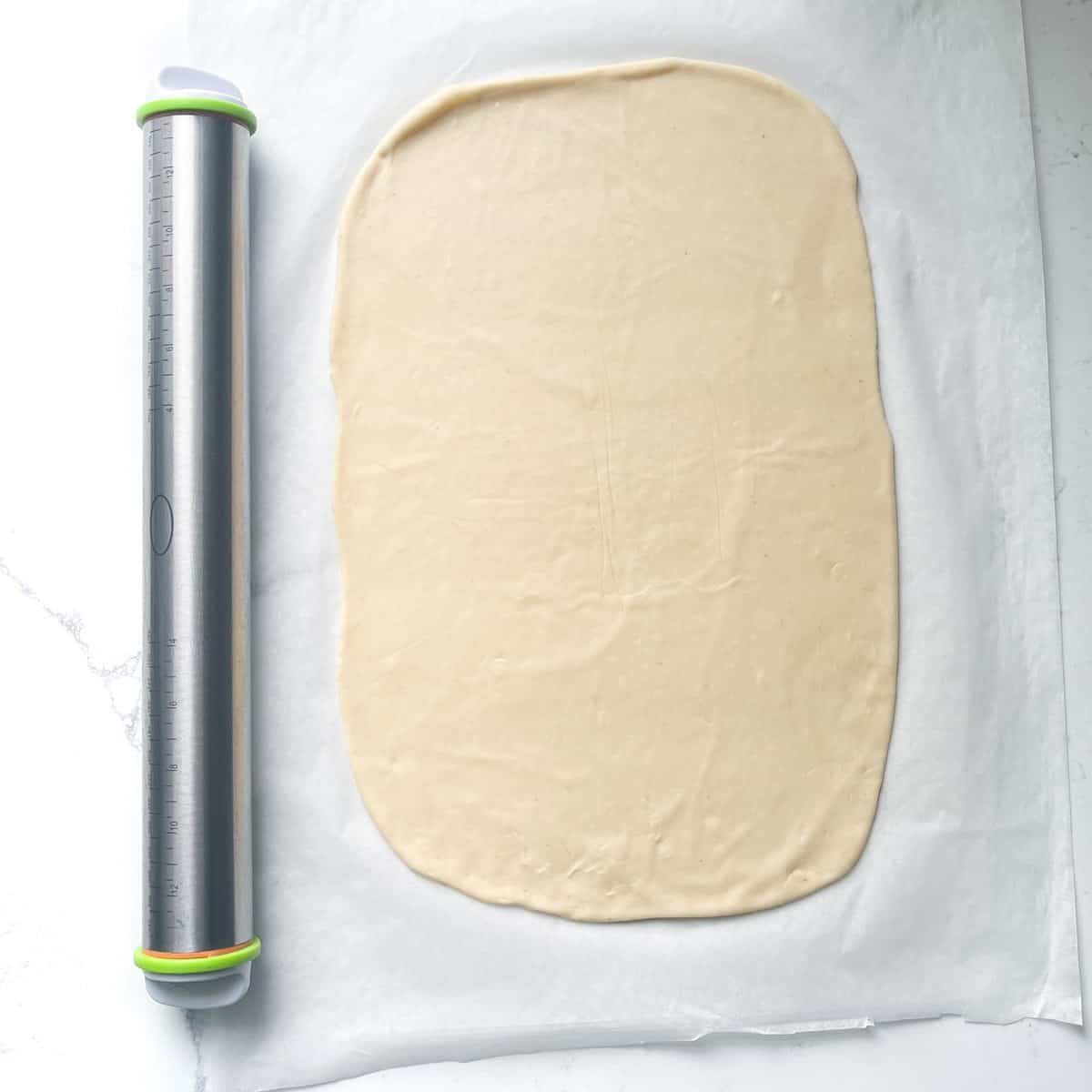 Rolled out pizza base for the flammkuchen in an oblong shape.